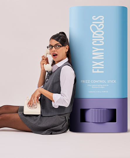 Woman posing with a phone next to 'Fix My Curls' Frizz Control Stick
