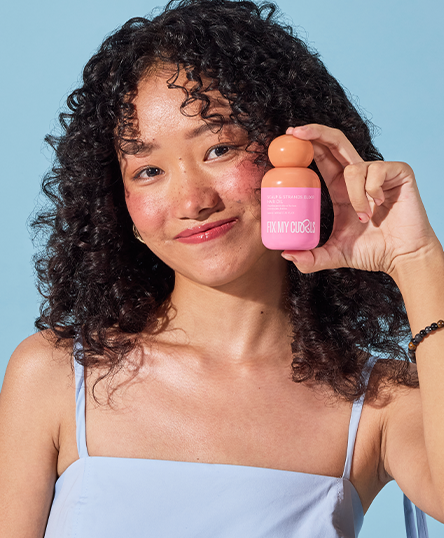 Woman holding Scalp & Strands Elixir Hair Oil in a blue background