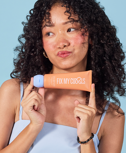 Woman holding Curl Quenching Hair Butter Tube of Fix My Curls against a blue background