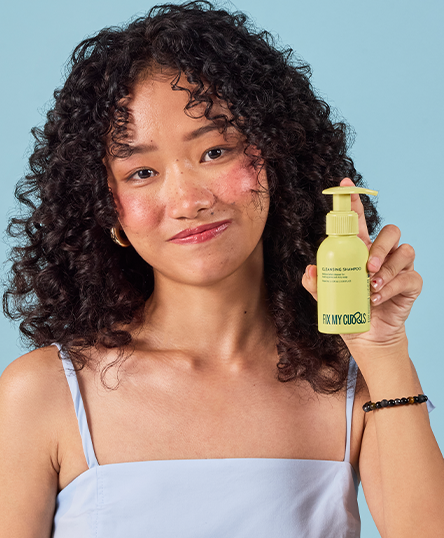 Woman holding a bottle of Cleansing Shampoo against a blue background