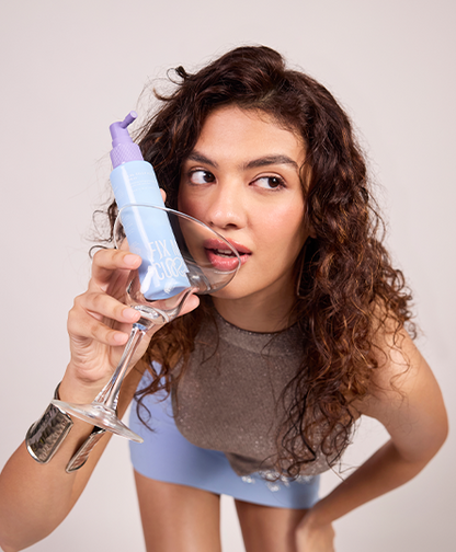 The model is posing with Fix My Curls'  Curl Gelly Activator spray in a glass